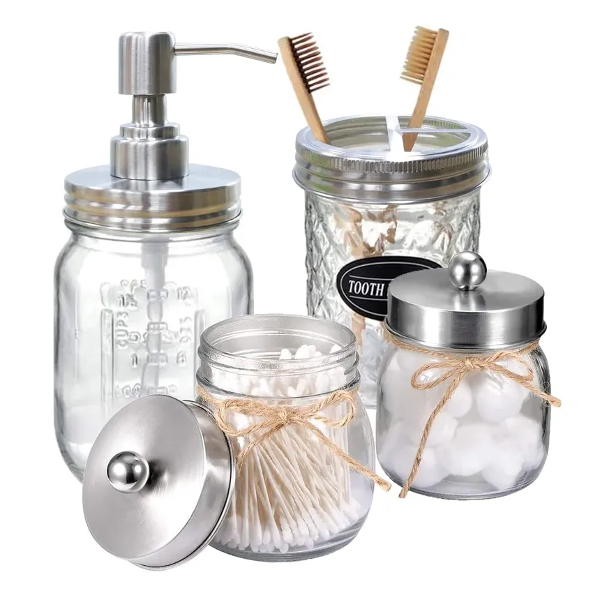 A set of glass jars for bathroom use, one with a pump dispenser, another labeled for toothbrush storage, and two with string-tied lids for cotton balls and swabs.