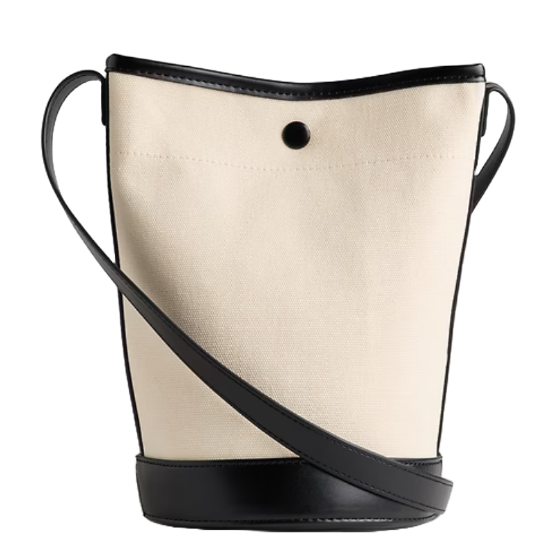 Beige canvas bucket bag with black leather accents and an adjustable crossbody strap.