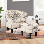 A barrel chair and ottoman with floral print and dark wood legs, on a multicolored area rug beside a round side table.