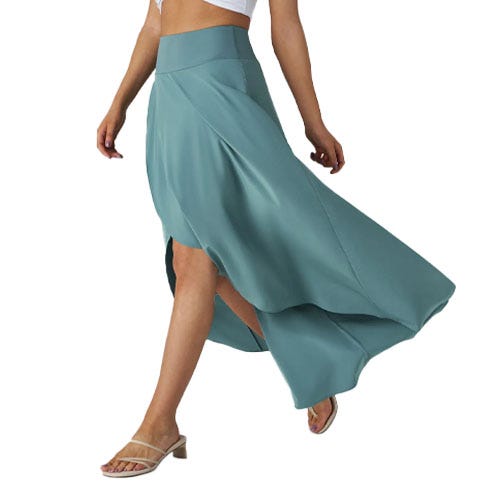 A person wears a flowing, teal-colored high-low skirt paired with a white crop top and strappy low-heeled sandals.