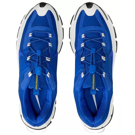 Blue athletic sneakers with a black and white sole, featuring a lace toggle system and \“Vomero\“ branding on the tongue.