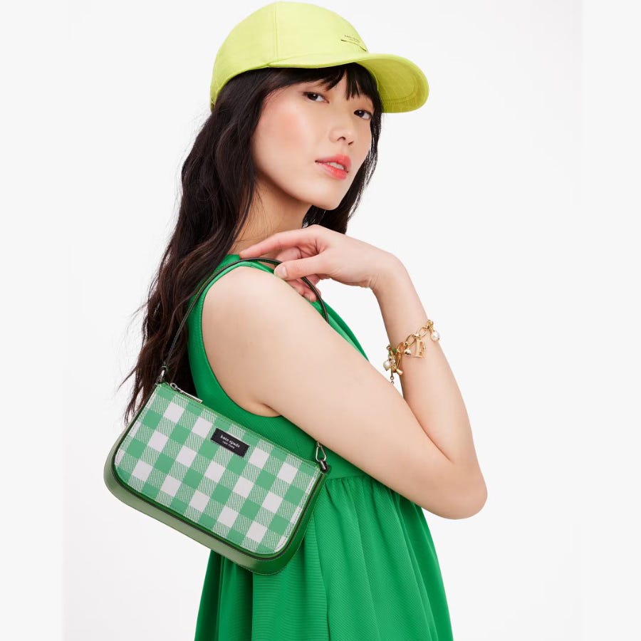 A woman is wearing a green cap and carrying a green and white checkered crossbody bag.