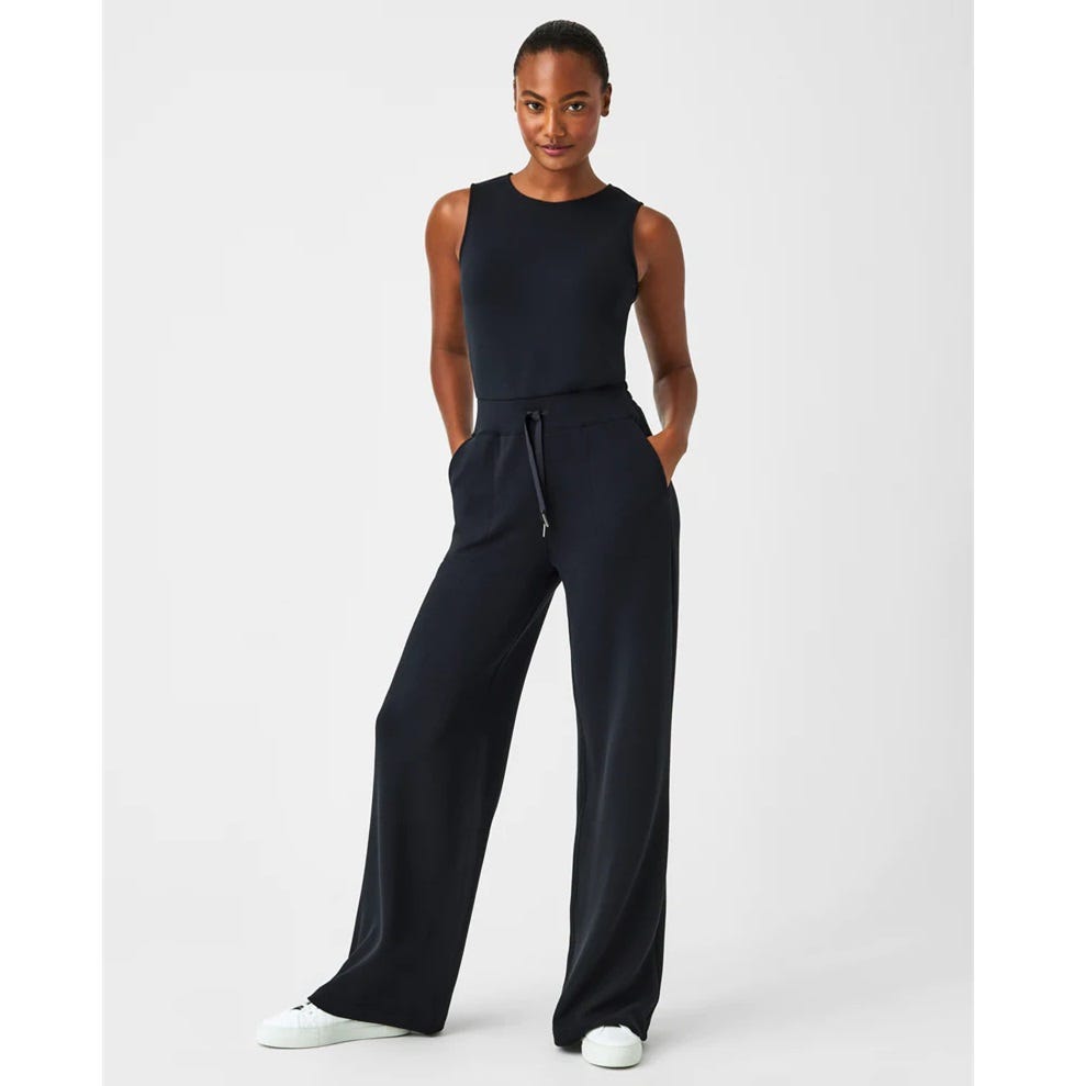 A woman is wearing a sleeveless navy jumpsuit with a drawstring waist and wide-leg trousers.
