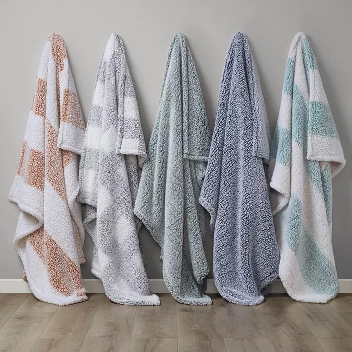 Five plush towels in varying colors of white, blue, and tan, displayed hanging side by side on hooks against a neutral wall.
