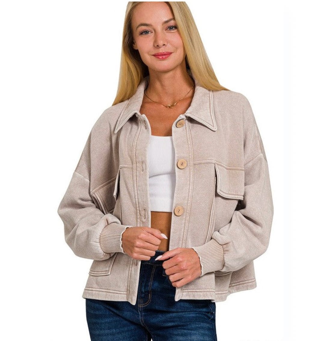 A woman is wearing a beige jacket with a collared neck and front pockets, paired with a white cropped top and blue jeans.