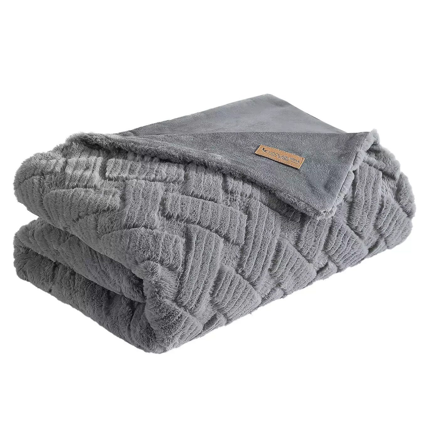 A soft gray, textured throw blanket featuring a herringbone pattern with a smooth, suede-like underside and a small leather tag sewn on one corner.