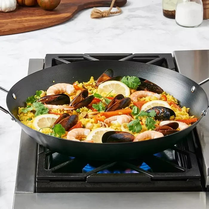 A paella with shrimp, mussels, lemon slices, and garnished with herbs in a large black pan on a stove.