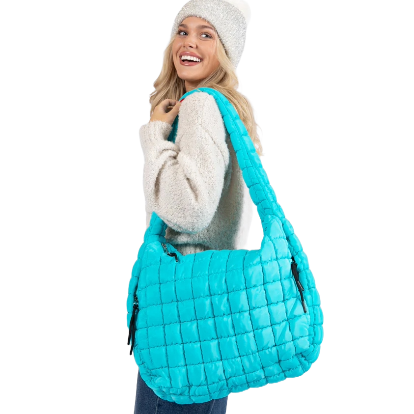 A smiling person wears a cozy sweater and knit hat, carrying a large, bright turquoise quilted bag with a wide strap.