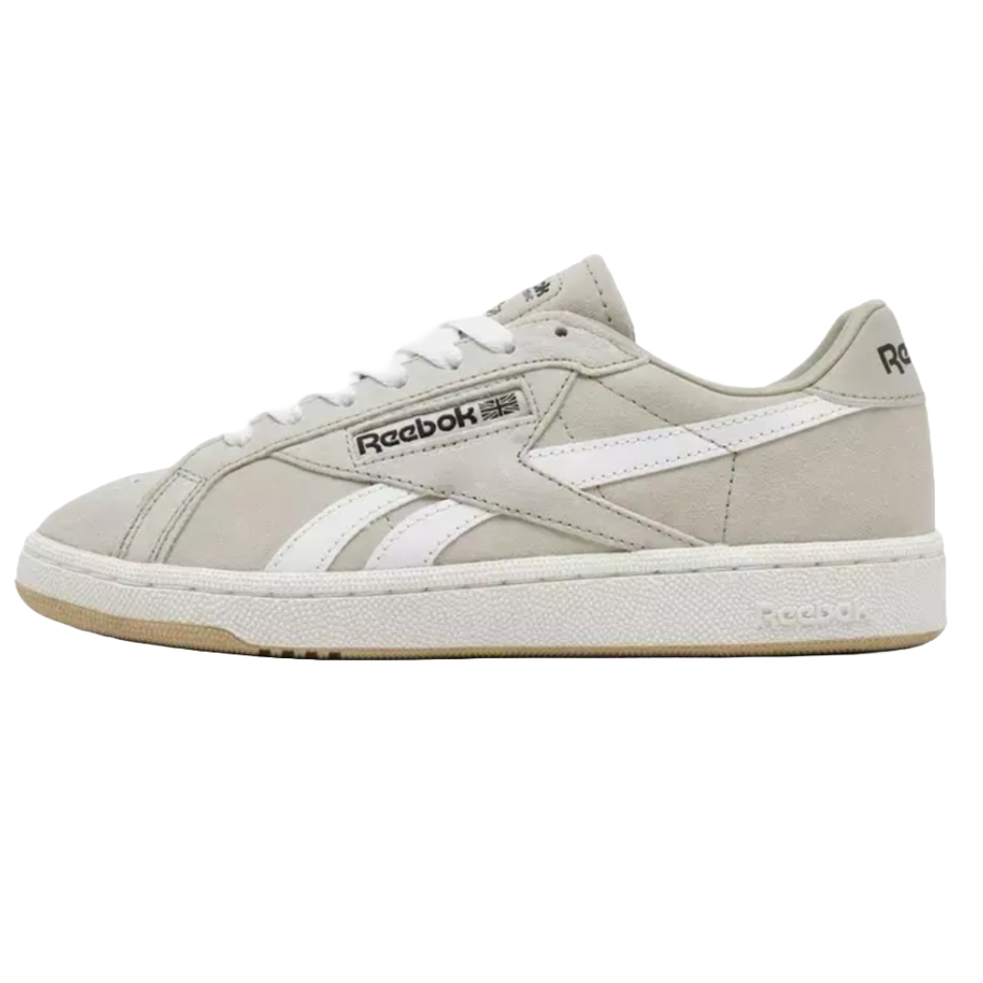 Reebok Club C Grounds UK Casual Shoes feature a classic low-top design with a light gray suede upper, white leather detailing, and a durable rubber sole. The Reebok logo is displayed on the side, tongue, and heel.