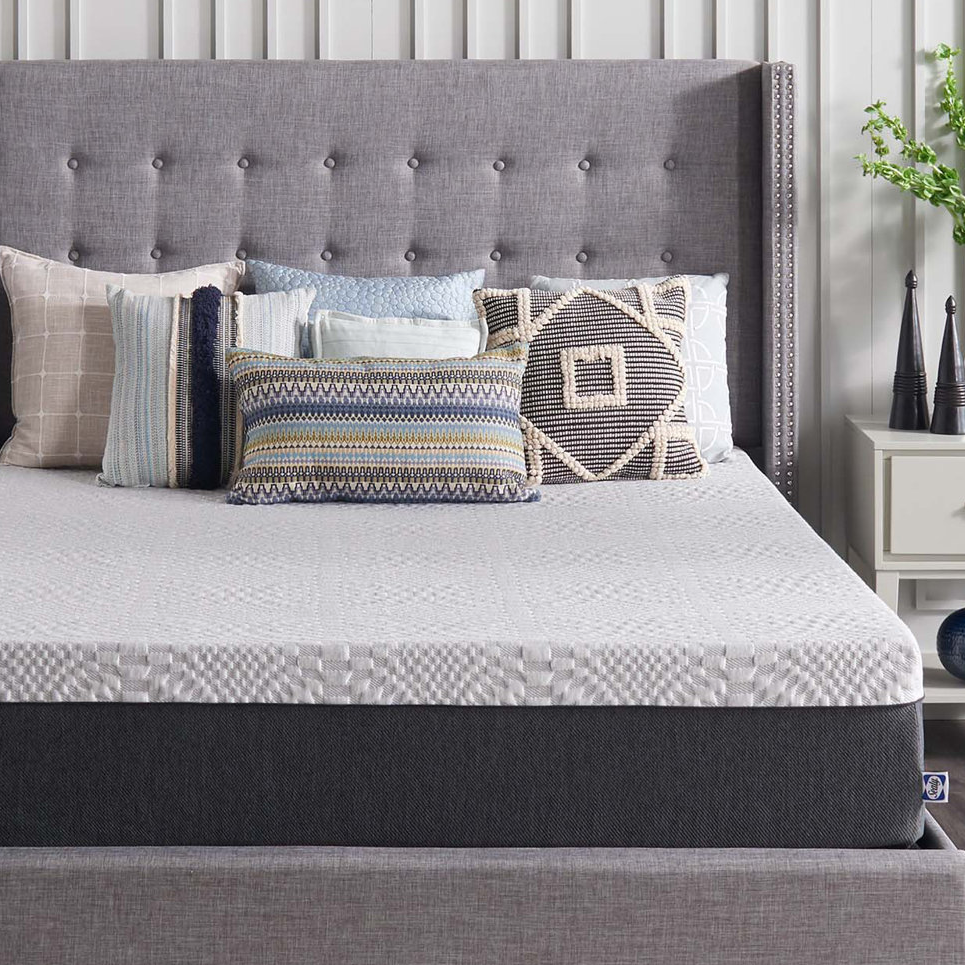 A gray upholstered bed with a diamond-patterned quilt and assorted decorative pillows in neutral and blue tones.