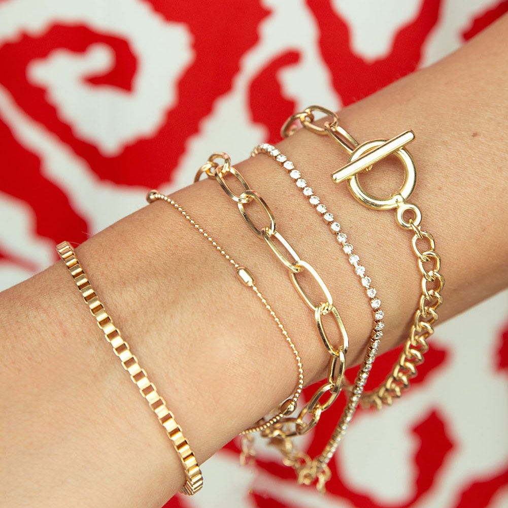 A collection of gold bracelets on a wrist, featuring different designs including chains and pearl embellishments.