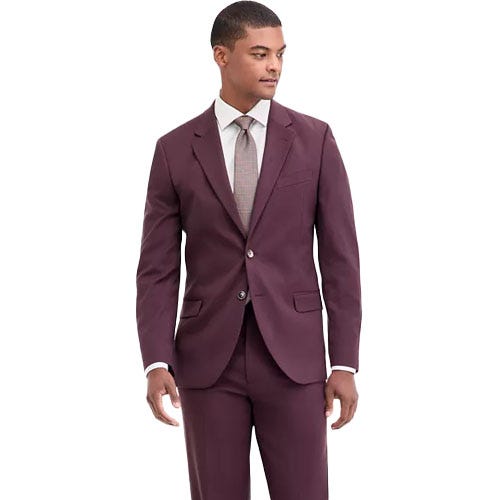 Man in a burgundy suit with a white dress shirt and patterned tie, standing against a plain background.