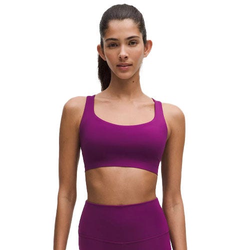 A woman wears a purple FlexyFlex Strappy Yoga Bra, featuring a simple and supportive design with wide straps and a scoop neckline, paired with matching high-waisted leggings.