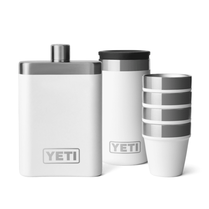 The Raise One Up Set includes a white YETI flask, a tumbler, and a stack of four cups with silver accents, designed for portability and sharing beverages.