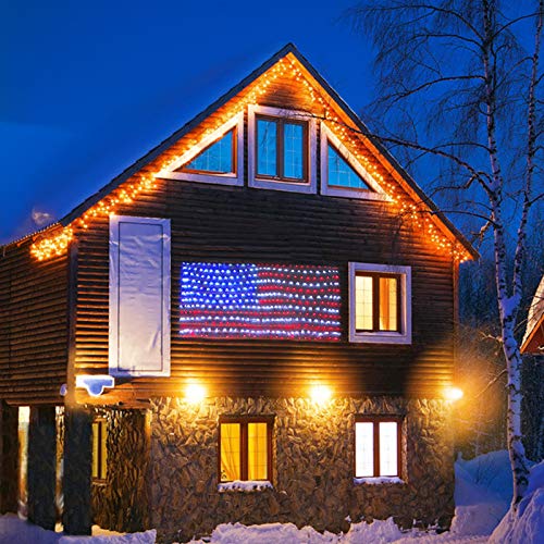 A large LED American Flag display with illuminated red, white, and blue lights is mounted on the side of a house at night.