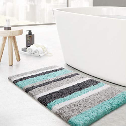 A striped bath mat with shades of teal, gray, and black lays on the floor beside a freestanding bathtub, offering a plush texture and anti-slip quality.