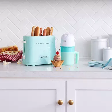 A turquoise Dash My Pint Ice Cream Maker is positioned on a kitchen countertop next to a hot dog toaster and other kitchen appliances.