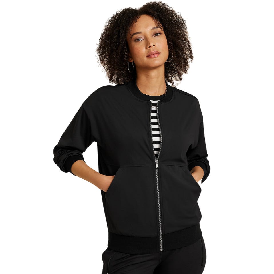 A woman wearing a black zip-up bomber jacket with pockets, over a black and white striped shirt, paired with black pants.