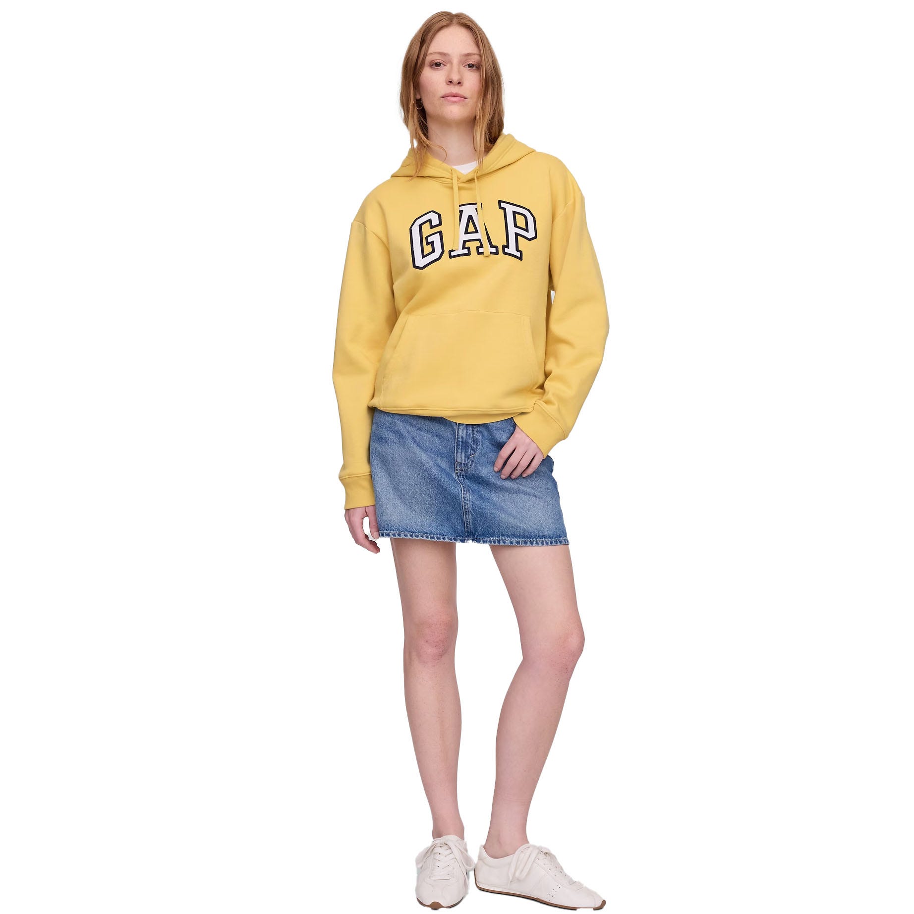 A person wears a yellow GAP hoodie paired with a denim mini skirt and white sneakers.