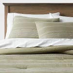 Striped green and white bedding set, including pillowcases and a comforter, on a bed with a wooden headboard.