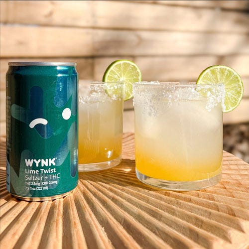 A can of WYNK Lime Twist Seltzer with THC next to two glasses of lime beverage garnished with lime slices.