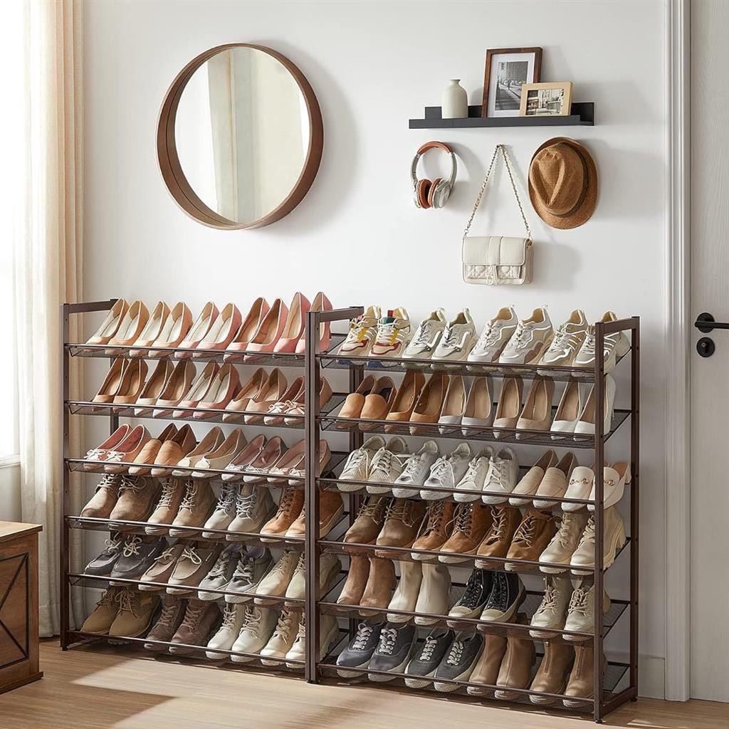 Multiple rows of shoes on shelves with a round mirror, shelf with personal items, and wall-mounted hooks with a hat and bag.