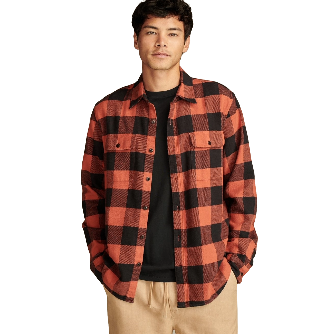 A man is wearing a Lucky Brand men's plaid flannel shirt in an orange and black pattern, paired with a black t-shirt and beige pants. The shirt features button closures and two chest pockets.