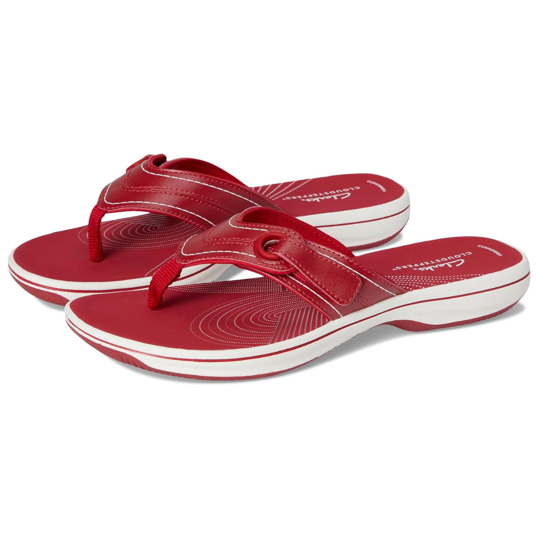 Clarks Breeze Sandals are red flip-flops with a comfortable cushioned footbed, featuring a toe post design and subtle concentric circle patterns on the insole. They have white accents on the sole, providing a stylish and casual look.