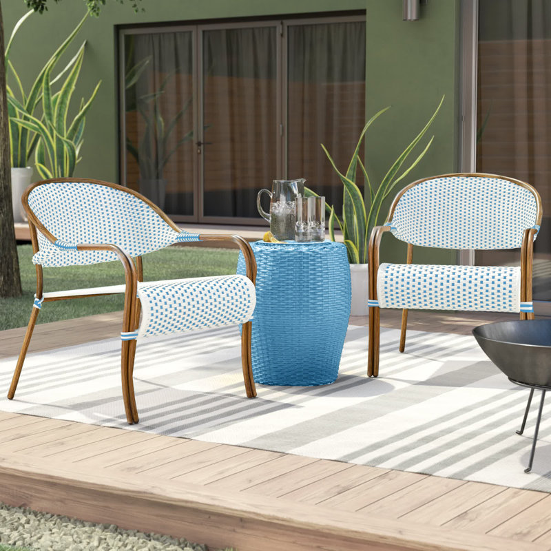 Outdoor furniture set comprising two chairs with blue and white patterned cushions, a matching small table, and a black metal bowl on a striped rug.