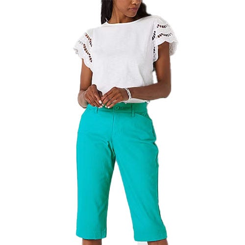 A woman is wearing a white short-sleeved top with eyelet details on the sleeves and teal knee-length pants.