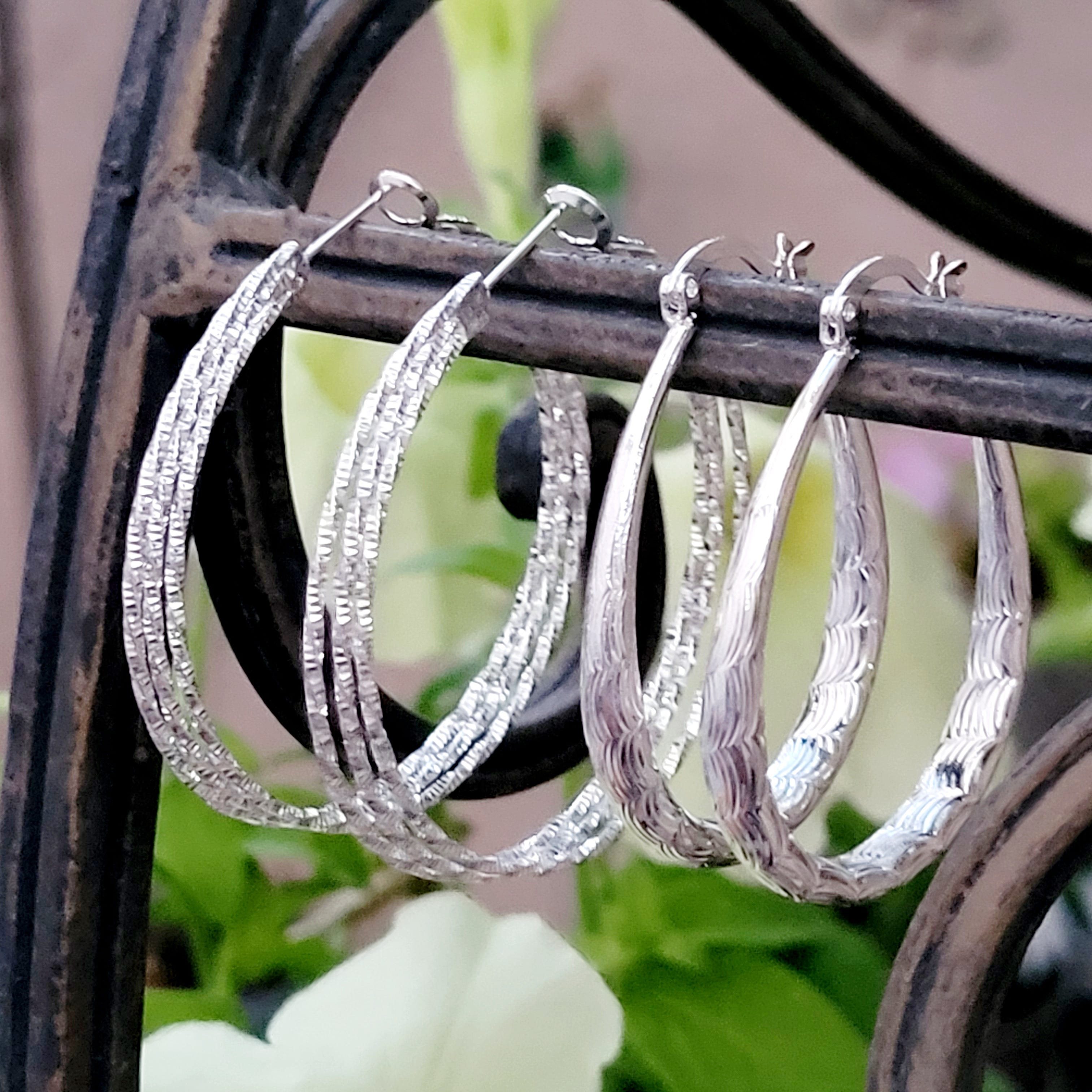 Three pairs of silver hoop earrings with different textures hanging from a metal stand.