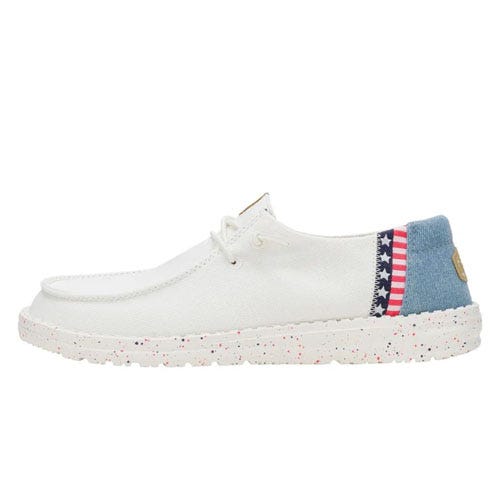 Hey Dude Wendy Americana Shoes feature a white canvas upper with a blue and star-striped heel detail, speckled white outsole, and a relaxed slip-on design with laces for a casual, patriotic look.
