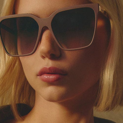 Large, square-framed sunglasses with a pale pink translucent frame and gradient tinted lenses, worn by a person with a blonde bob haircut.
