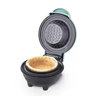 A teal Dash Mini Waffle Bowl Maker is open, revealing a freshly cooked waffle bowl inside its round, grid-patterned cooking plate.