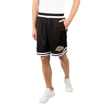 A person is wearing black basketball shorts with white stripes and a team logo, paired with white sneakers.