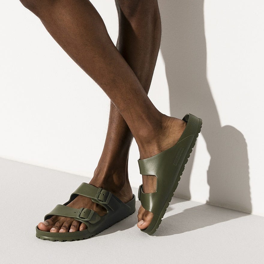 A pair of green slide sandals with adjustable straps is shown on a person's feet.