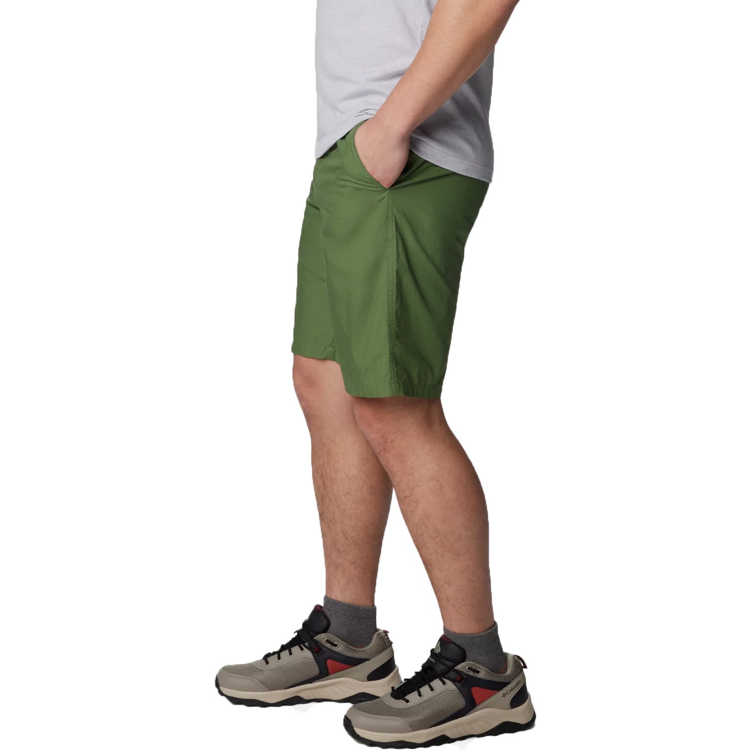 Green knee-length men's shorts with a pocket on the right thigh, paired with a gray t-shirt and gray hiking shoes with red accents.