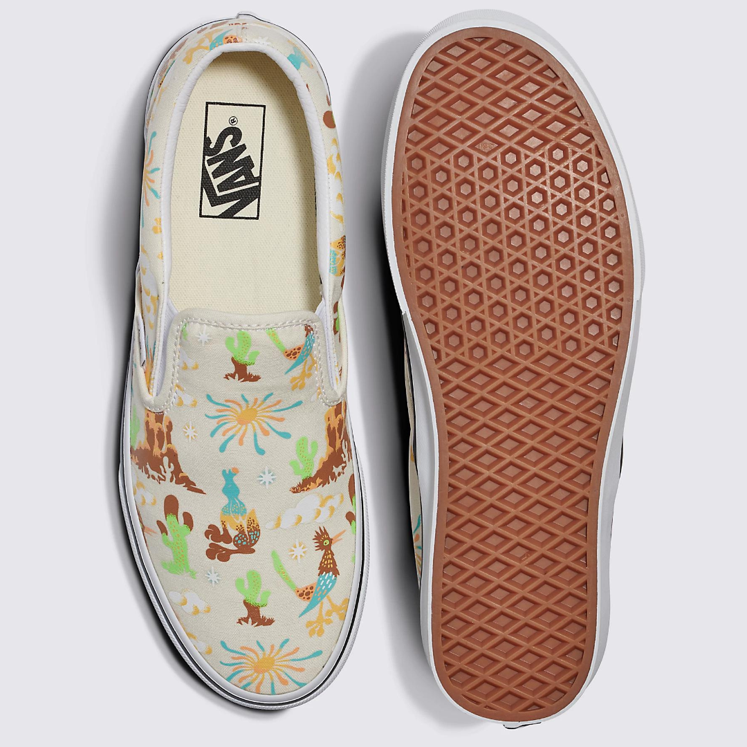 A pair of slip-on sneakers with a colorful dinosaur and plant print, and a brown waffle-patterned sole.