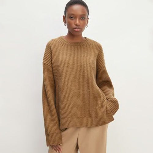 A woman wearing a brown ribbed sweater and light beige pants.