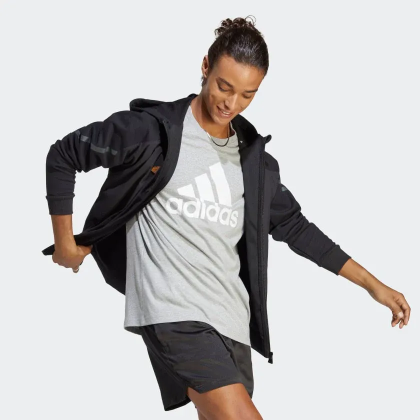 A person wearing a grey t-shirt with Adidas logo, black shorts, and a black jacket.