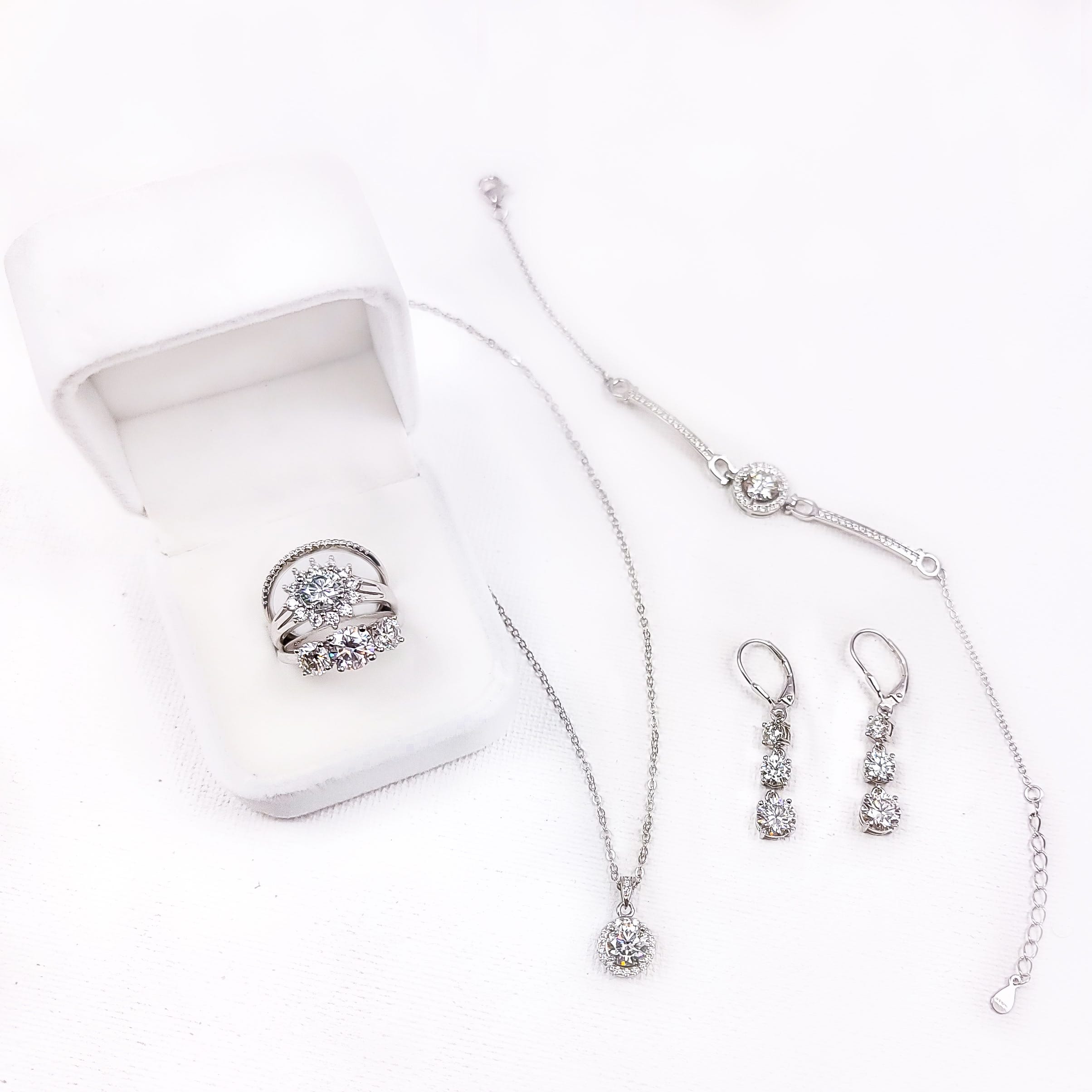 A set of diamond jewelry including a ring in a box, a pendant necklace, a bracelet, and drop earrings on a white background.
