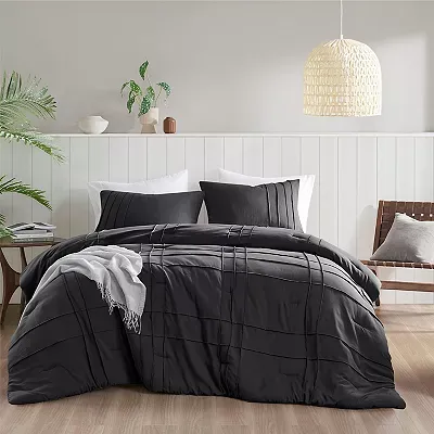 A black queen comforter set with pleated design, accompanied by two matching pillow shams on a bed within a simply decorated room.