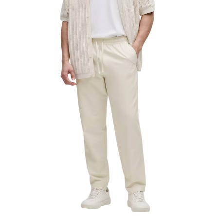 A person is wearing beige drawstring pants, a white T-shirt, a matching knitted short-sleeve sweater, and white sneakers.