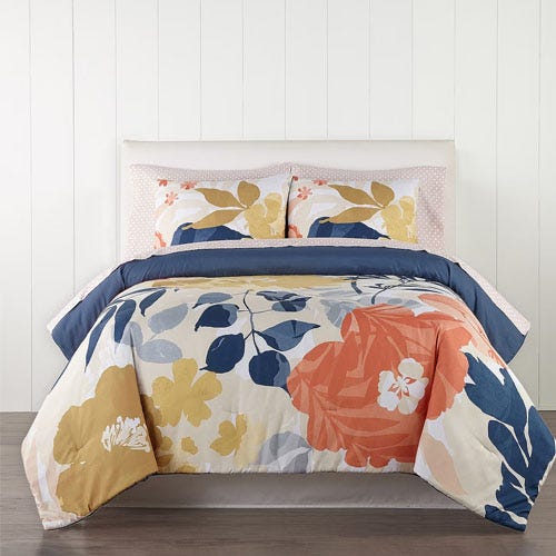 A floral patterned bedding set with coordinating pillows on a bed against a white panelled wall.