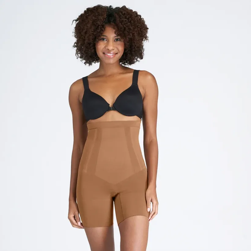 A woman wearing a black bra and high-waisted beige shapewear shorts.