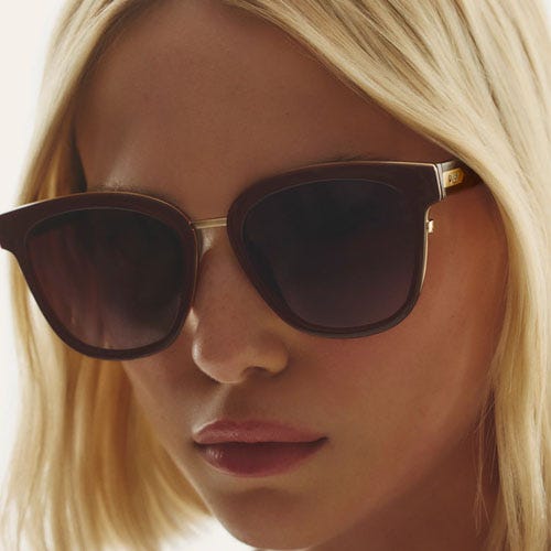 A woman wearing oversized sunglasses with dark tinted lenses and a gold-tone frame.