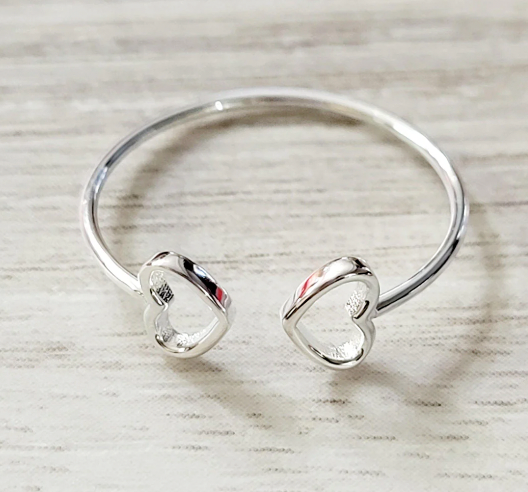 A thin silver ring features two open heart shapes at its ends, creating a delicate and minimalist design.