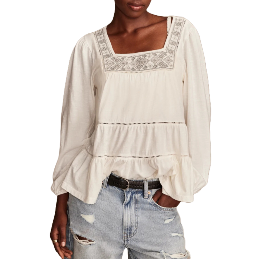 Cream-colored square neck top with patterned embroidery on the neckline, long sleeves, and a loose, tiered design. Paired with light blue ripped jeans.