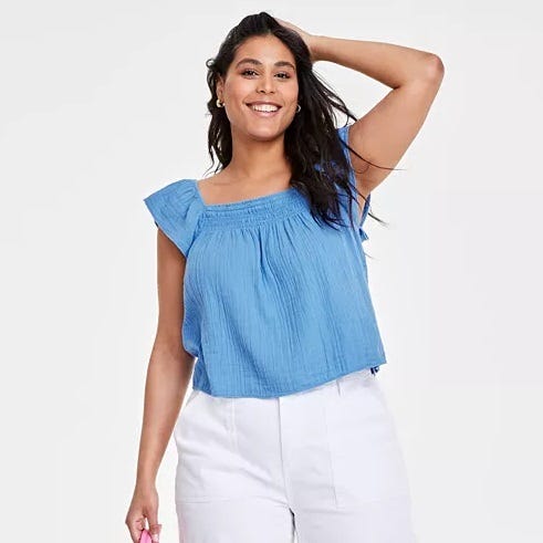 A woman is wearing a light blue sleeveless blouse with ruffle details and white pants.