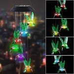 A solar LED hummingbird wind chime featuring multiple acrylic hummingbirds that cycle through a variety of colors when lit up, suspended from a black top housing the solar panel.